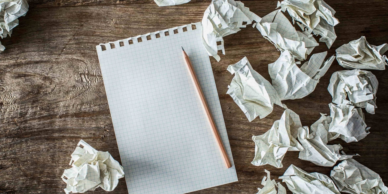 A blank sheet of rectangular paper with a pencil on a wooden background with scrunched up pieces of paper surrounding it
