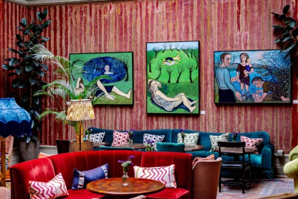 A red walled room furnished with sofas and furnishings in red, teal, blue and green. Three works of art hang from the wall.