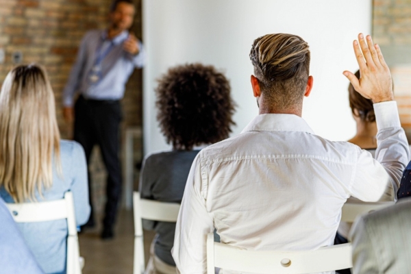 Back view of a man with short blond hair asking a question on a seminar.