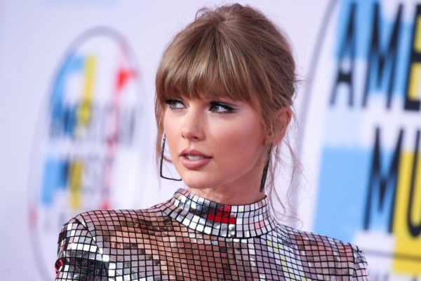 A portrait of Taylor Swift at an event look off camera. She is white with long blond hair and wears a silver sparkly dress.