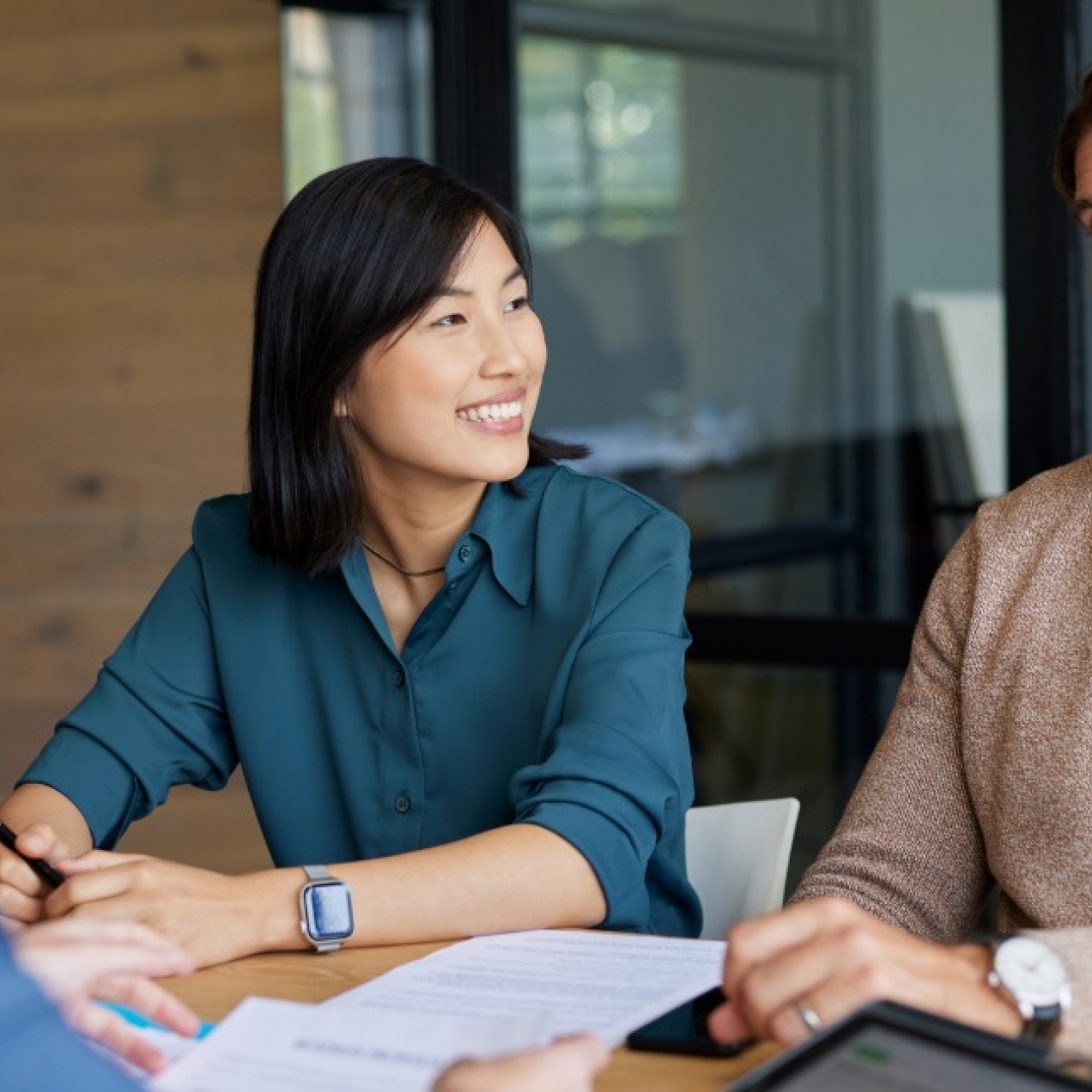 An Asian woman and a white man sit smiling on one side of a board table. Opposite them is the obscured view of another woman