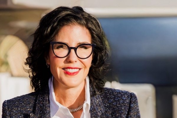 A colour photograph of Tina Fordham, who is a white woman with dark hair and glasses, wearing a grey jacket over a white shirt.