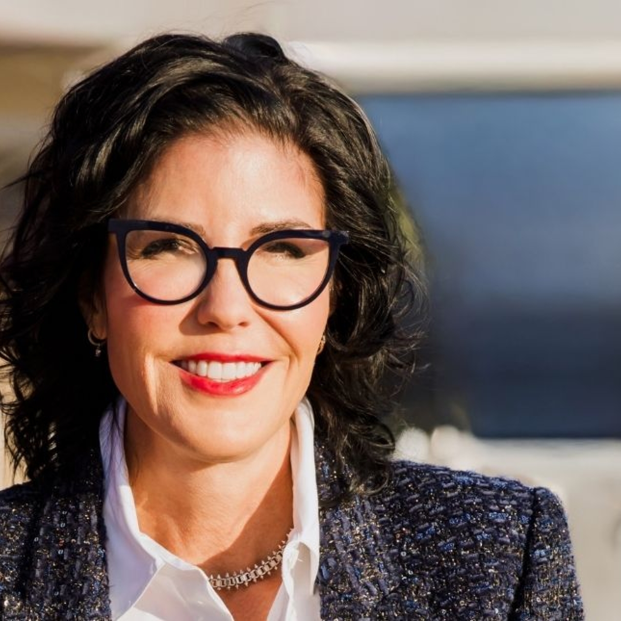 A colour photograph of Tina Fordham, who is a white woman with dark hair and glasses, wearing a grey jacket over a white shirt.