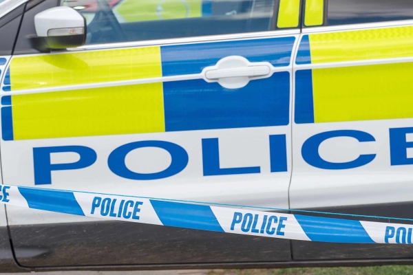 Close up shot of a police car door with blue and white police tape in the foreground