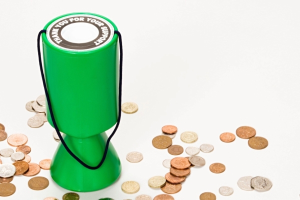 A green charity collection box sits on a white background with coins scattered all aournd it