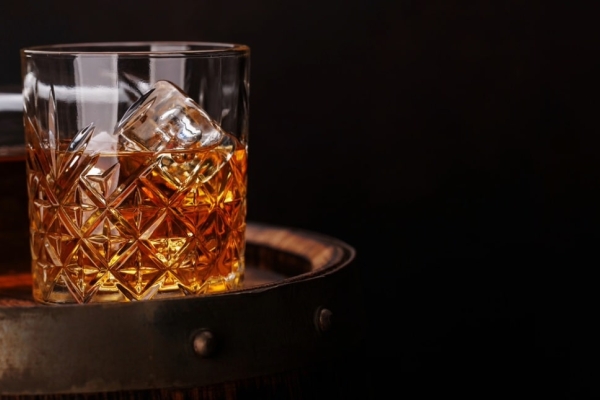 On a black background a glass of whisky stood on the top of an aged barrel.