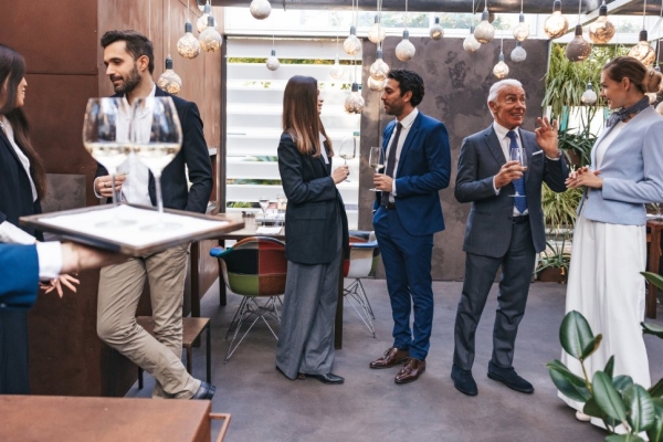 Five professionals of different ages holding wine glasses while networking in a modern event space