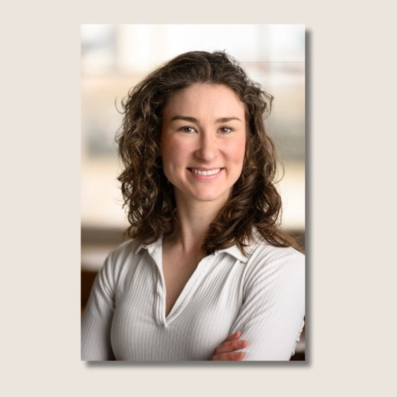 A colour portrait of Zenia Duell. Zenia is a white woman with long, dark curly hair who is looking at the camera and smiling