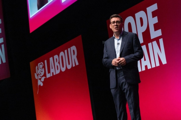 Andy Burnham on stage against a pink-red backdrop.