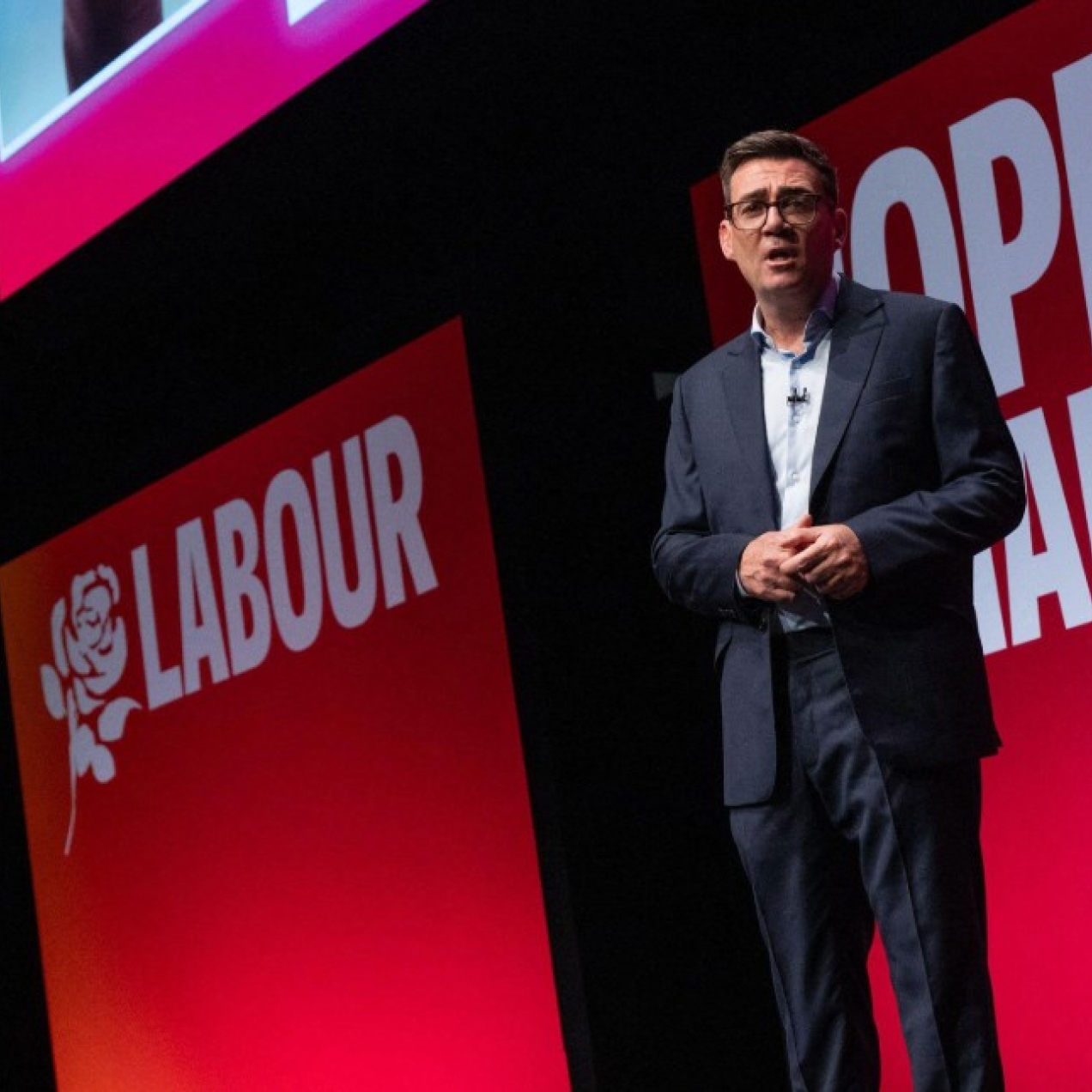 Andy Burnham on stage against a pink-red backdrop.