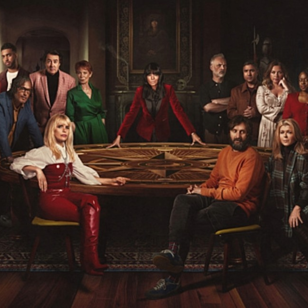 A BBC publicity photo of Claudia Winkleman and the cast of Celebrity Traitors in a darkened room around a table