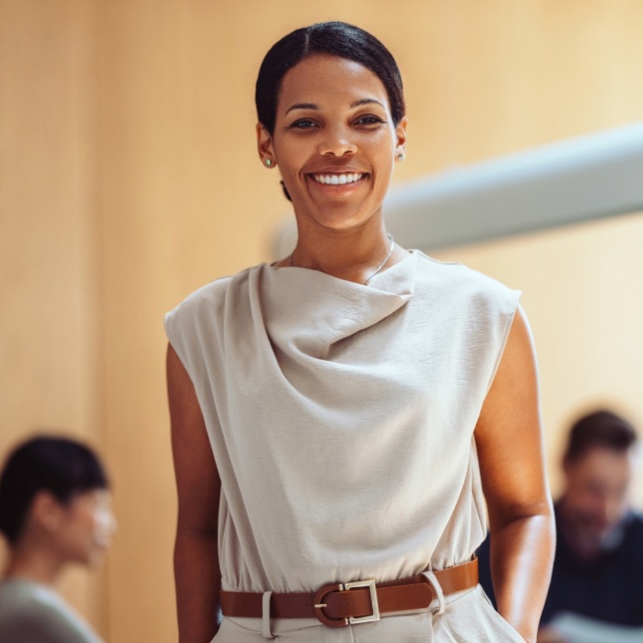 A smiling Black female business leader. Three colleagues, who are out of focus, are sat in the background.