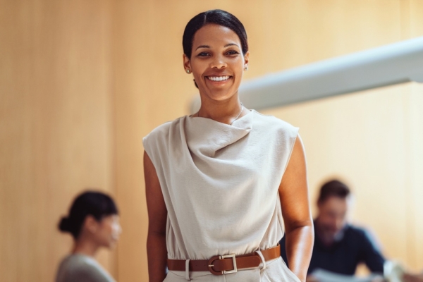 A smiling Black female business leader. Three colleagues, who are out of focus, are sat in the background.