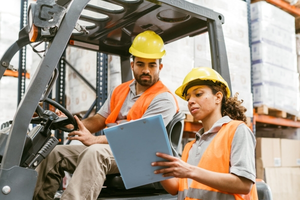 A woman warehouse manager giving instructions to a male forklift operator