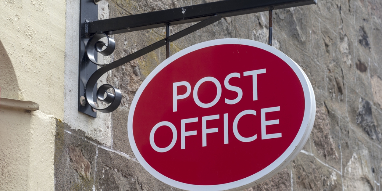A red oval post office sign attached to a stone building
