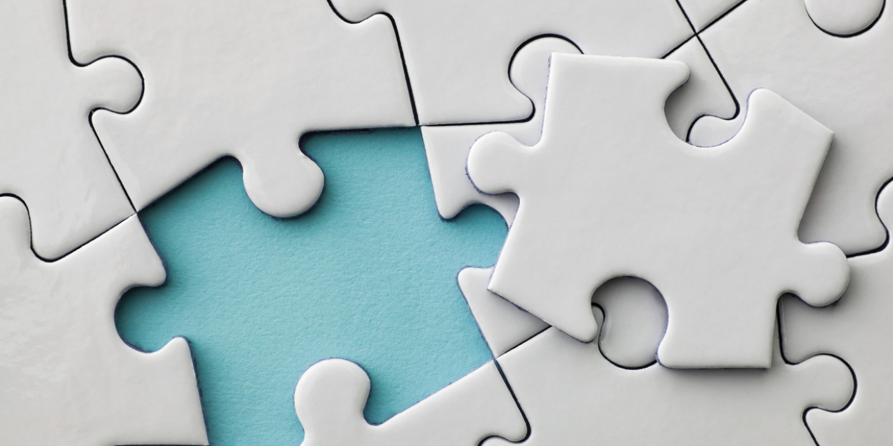 Close up of a plain off-white jigsaw puzzle. The final piece is placed on top of the others, with a turquoise background showing where the space where is to be inserted