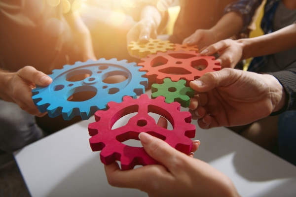 Six hands holding four cogs of various sizes together