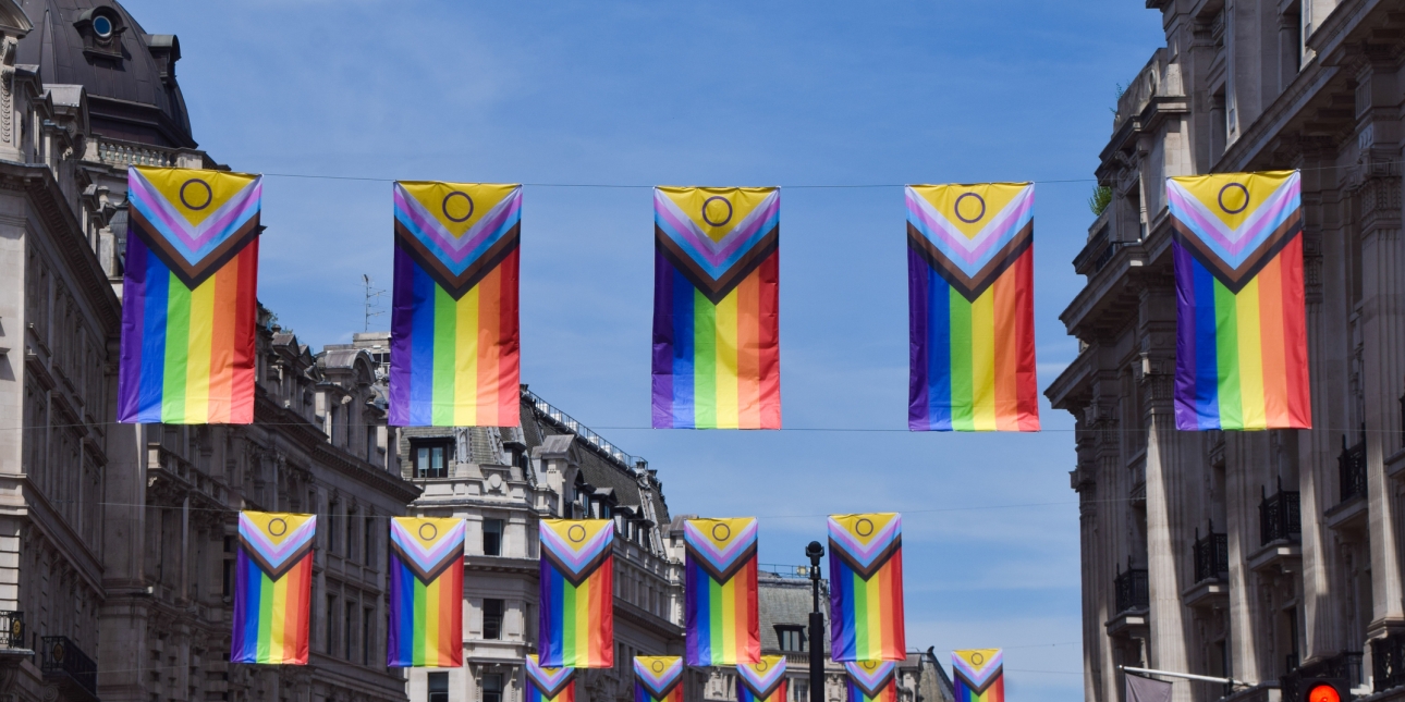 Four rows of five sets of Pride flags hanging between buildings on Regent Street in London set against a blue sky