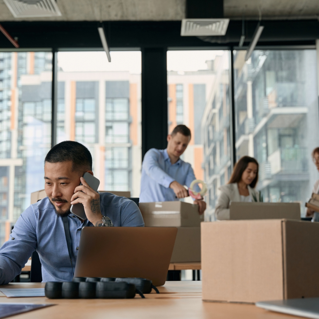 Office worker on the phone while surrounded by boxes. Three colleagues in the background packing boxes.