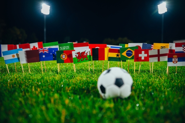 A football on grass. In the background are flags of the participating football team's countries.