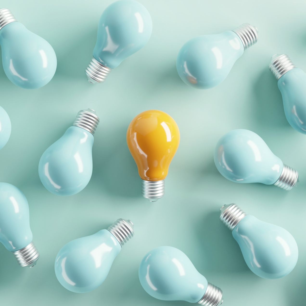 A bird's eye view of a yellow tinted light bulb laid flat on a teal background, surrounded by 15 turquoise-tinted bulbs
