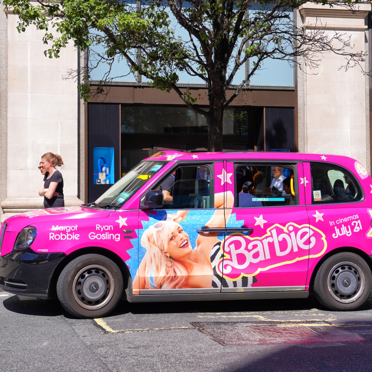 A pink London taxi with Barbie advertising on the side. It includes an image of Margot Robbie