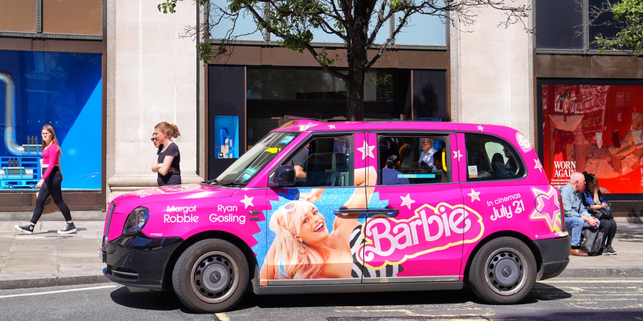 A pink London taxi with Barbie advertising on the side. It includes an image of Margot Robbie