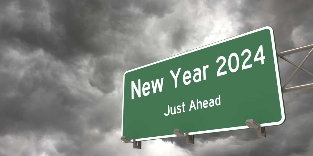Grey storm clouds surround a green traffic sign, fixed to a gantry, which features the words New Year 2024 just ahead