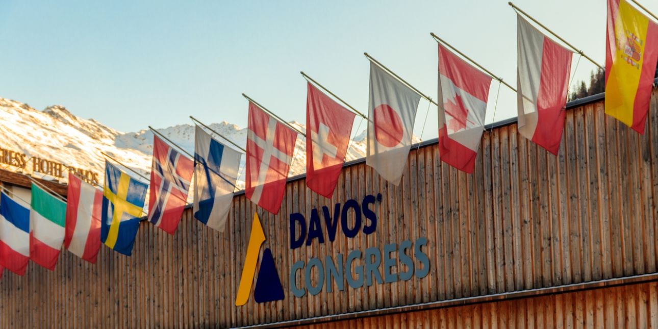 Close up exterior shot of Davos Congress Centre with flags displayed along it and snowy mountains in the background