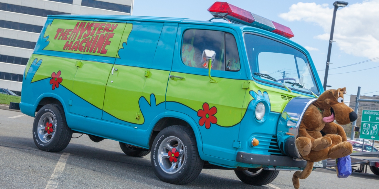 A van painted in blue and green with the words Mystery Machine on the side to emulate the van in the Scooby Doo cartoon. A soft toy Scooby Doo sits in the middle of the spare tyre at the front.