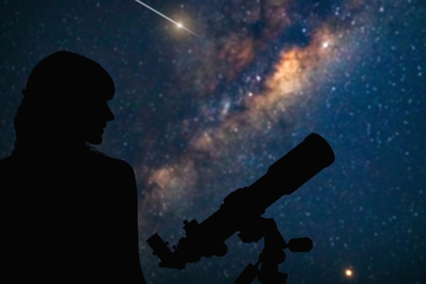 A silhouette of an astronomer and a telescope against a star filled sky