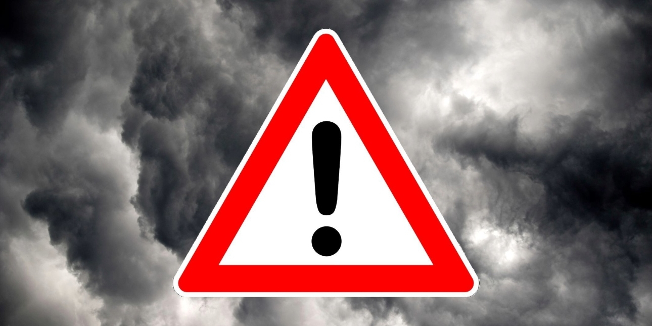 On a background grey storm clouds, sits a computer generated image of a warning sign. This is composed of a black exclamation mark inside a red-outlined white triangle.