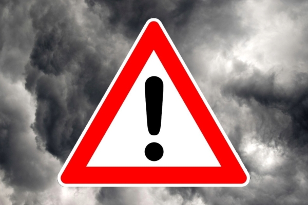 On a background grey storm clouds, sits a computer generated image of a warning sign. This is composed of a black exclamation mark inside a red-outlined white triangle.