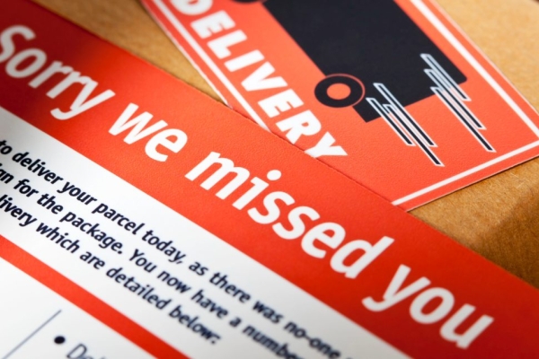 A red missed delivery card placed on top of a cardboard box that features a delivery sticker.