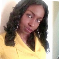 A colour portrait of Amina Maikori looking side on at the camera. Amina is a Black woman with dark shoulder length hair, who wears a yellow top and hooped earrings.