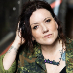 A colour portrait of Dannie-Lu Carr, a white woman with dark hair wearing a camouflage jacket