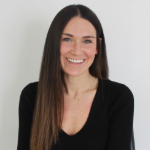 A colour portrait of Georgia Entrican smiling against a grey background. Georgia is a white woman with long dark hair, wearing a black top.