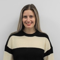 A portrait of a smiling Helen Salving against a grey background. Helen is a white woman with long brown hair and wearing a horizontal black and cream striped jumper