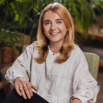 A portrait of Isabella Goldstein sat in a chair. Isabella is a white woman with long hair and a white top.