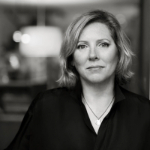 A black and white portrait of Juliet Warkentin. Juliet is a white woman with blond hair wearing a black top.