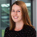 A colour portrait of Michelle Langley smiling. Michelle is a white woman with long red hair who wears a dark top.