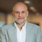 A colour portrait of Ronn Torossian. Ronn is a white man with grey beard who wears a grey jacket over a white shirt.