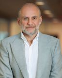 A colour portrait of Ronn Torrissian. Ronn is a white man with greying beard, wearing an open neck white shirt under a grey suit jacket