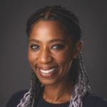 Head and shoulders of Terri McCollin, a Black woman with braided hair. She is looking at the camera and smiling. The background is dark grey.
