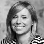 A black and white portrait of Lysanne Currie smiling at the camera. Lysanne is a white woman with brown hair. She wears a striped top.