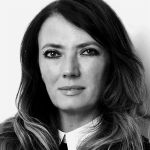 A black and white headshot of Joely Carey. Joely is a white woman with long dark hair.