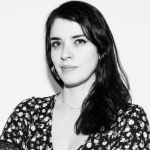 A black and white portrait of Sara Nelson. Sarah is a white woman with long dark hair wearing a patterned top.