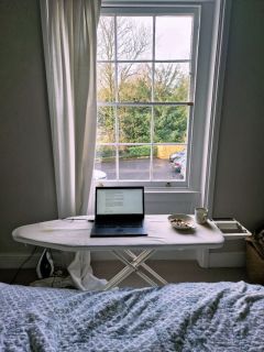 Mat Gazeley's laptop, bowl of cereal and mug perched on an ironing board next to a bed. There is a window in the background.