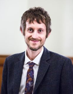 Leigh Greenwood, a white man with dark hair and beard, wearing a navy blazer and tie