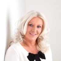 Jane Hunt, a white woman with blonde shoulder length hair, wearing a white top with black bow on the neck line